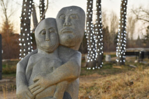 A stone sculpture of a parent and child embracing, set against a backdrop of trees adorned with white lights, capturing a tender moment in a tranquil outdoor setting.